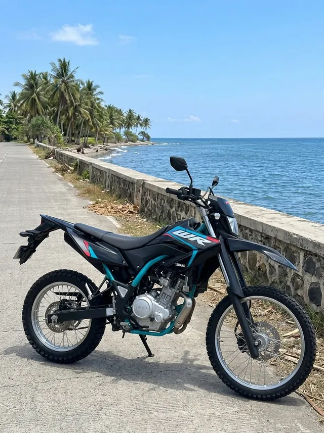 Yamaha WR155 trail bike in black and teal, available for self-ride rental in Bali, on a coast road by the sea